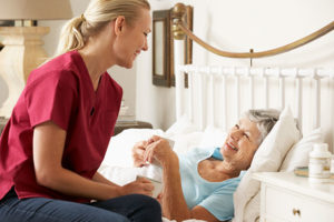 An older woman smiles at the caregiver at her bedside as they each hold a cup of tea.