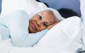A woman lies in bed with a frustrated look on her face, experiencing sleeping problems in dementia.