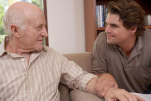 An older man looks angrily at a younger man, who has placed a hand on his arm as he attempts to calm aggressive behaviors in dementia.