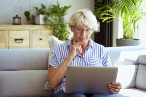 A mature woman who is working and caregiving looks thoughtfully at her laptop to find the help she needs.