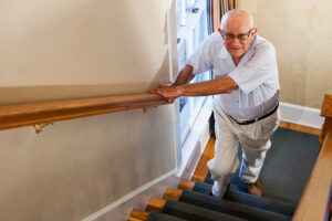 A man displays one of the early signs of mobility problems in older adults as he grips the railing tightly with both hands while making his way up a set of stairs.