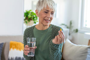 A woman who knows the most important vitamins for older adults holds a glass of water and a supplement she is preparing to take.