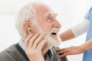 A man who knows about the link between hearing loss and dementia smiles as he uses a hearing aid.