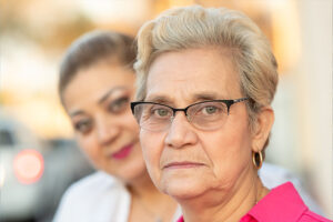 A woman who needs family caregiver support stands behind the older woman in her care.