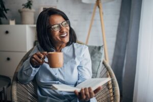 A woman who has let go of caregiver guilt enjoys a cup of coffee while reading a book.