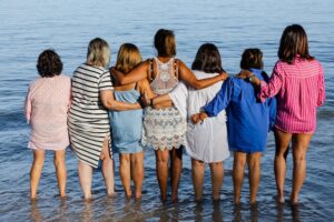 A group of women who know the importance of supporting family caregivers wrap their arms around each other as they face the ocean.
