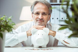 A man smiles confidently as he leans on a piggy bank, symbolizing overcoming financial concerns after a dementia diagnosis.